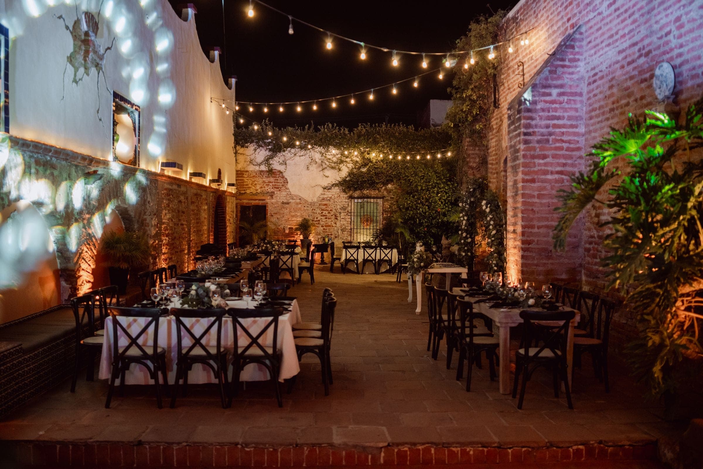 A courtyard laid with tables under strung lights in the evening