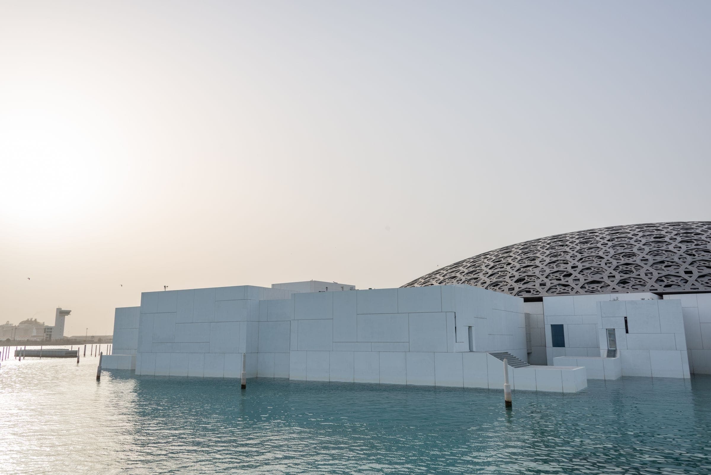 A low domed museum building standing over still water in haze
