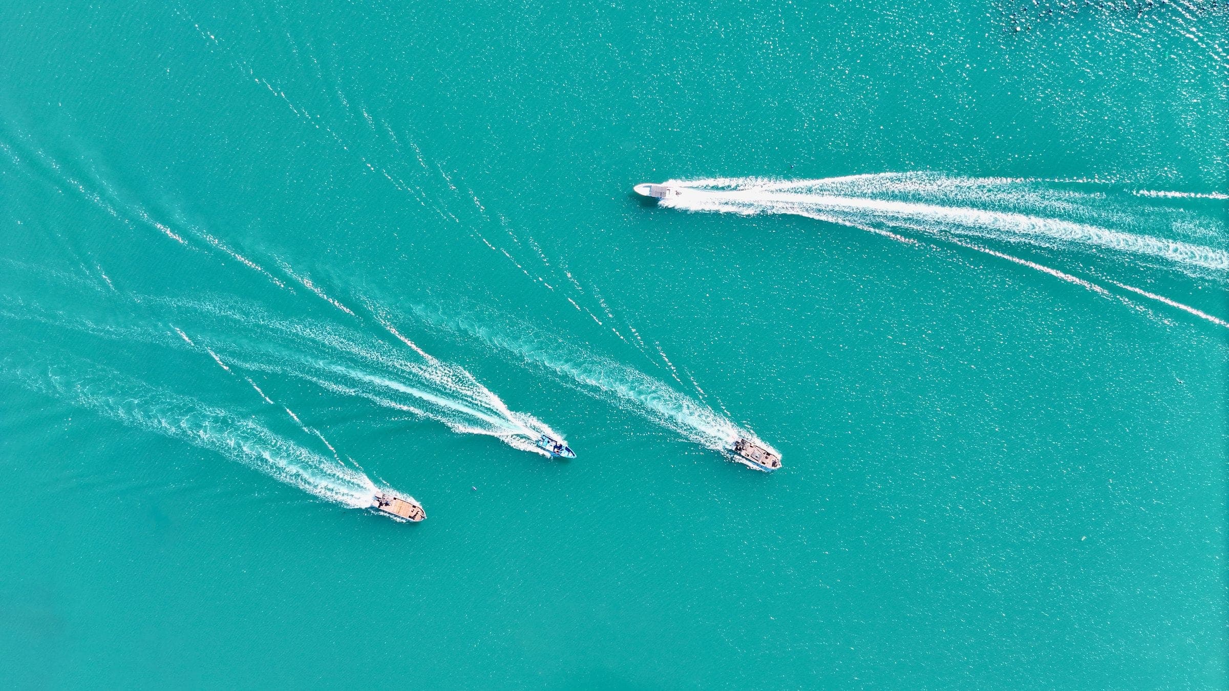 Two boats crossing bright turquoise shallows, seen from the air