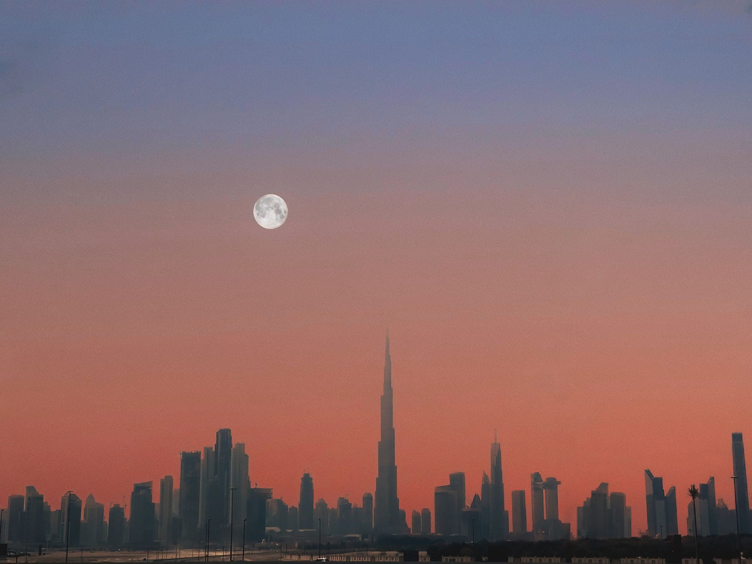 The Dubai skyline in silhouette at dusk beneath a rising moon