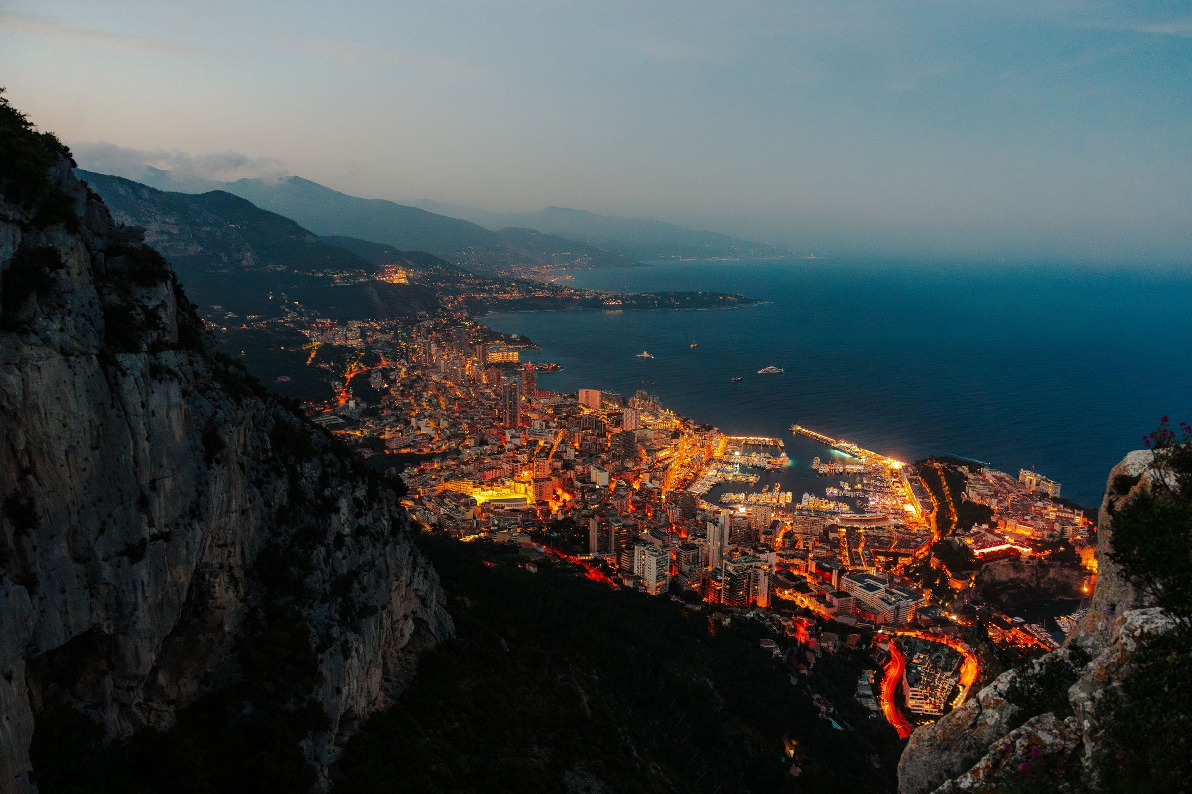 A Riviera city and harbour at night, seen from the hillside above