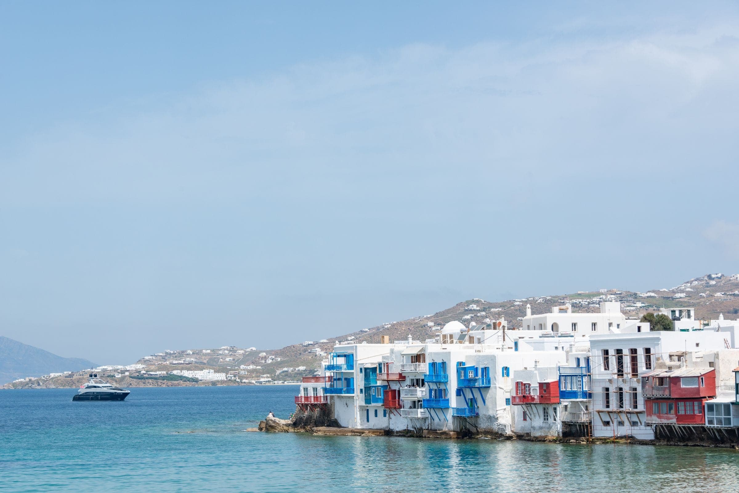 Whitewashed houses standing at the water’s edge on a Cycladic waterfront