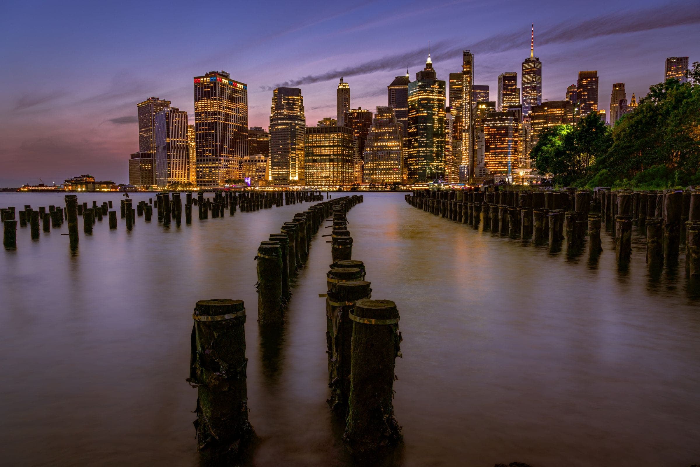 Lower Manhattan at dusk across the water, old pier pilings in the foreground