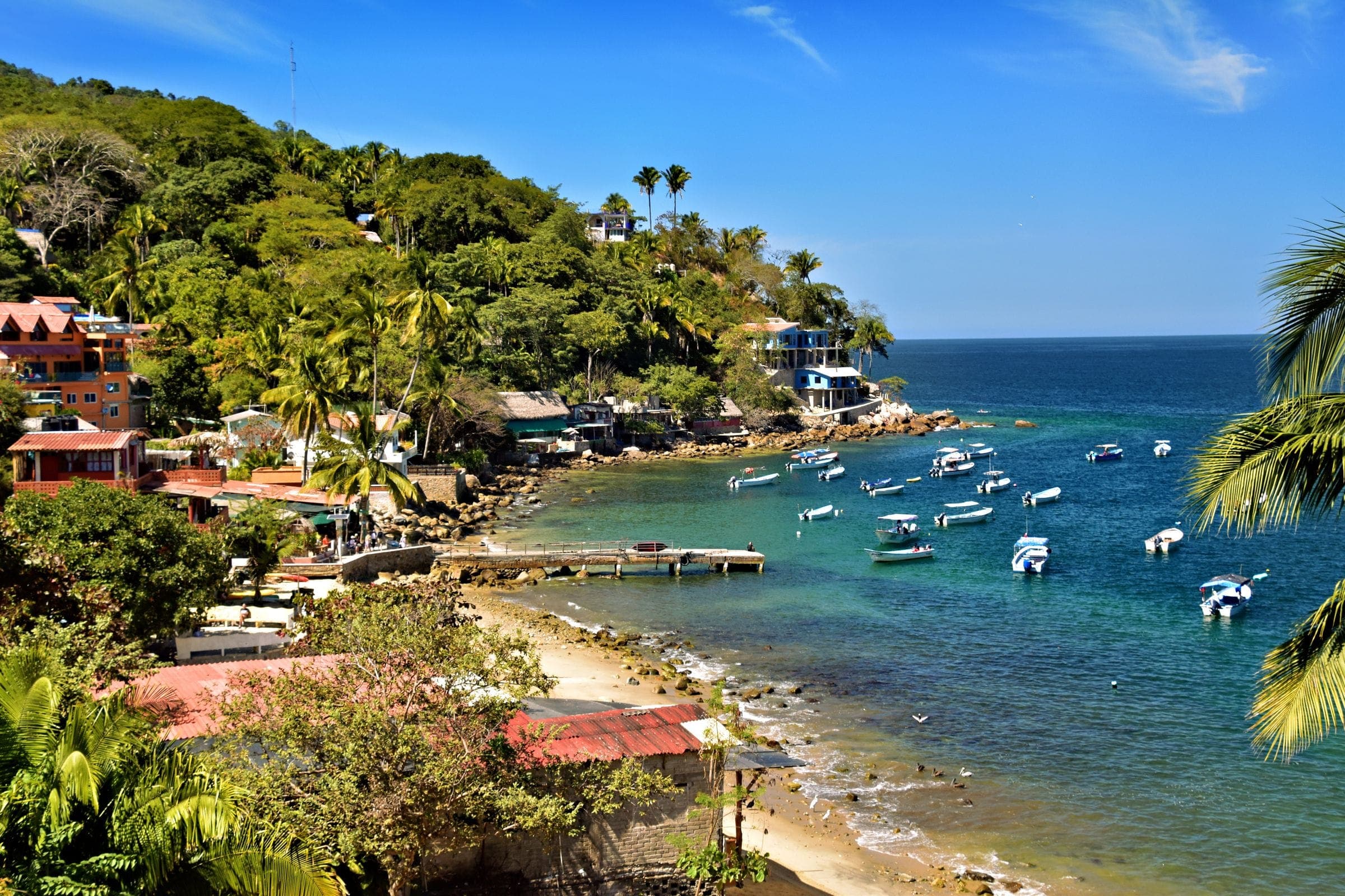 A Pacific bay in Mexico with small boats and jungle-covered hills behind