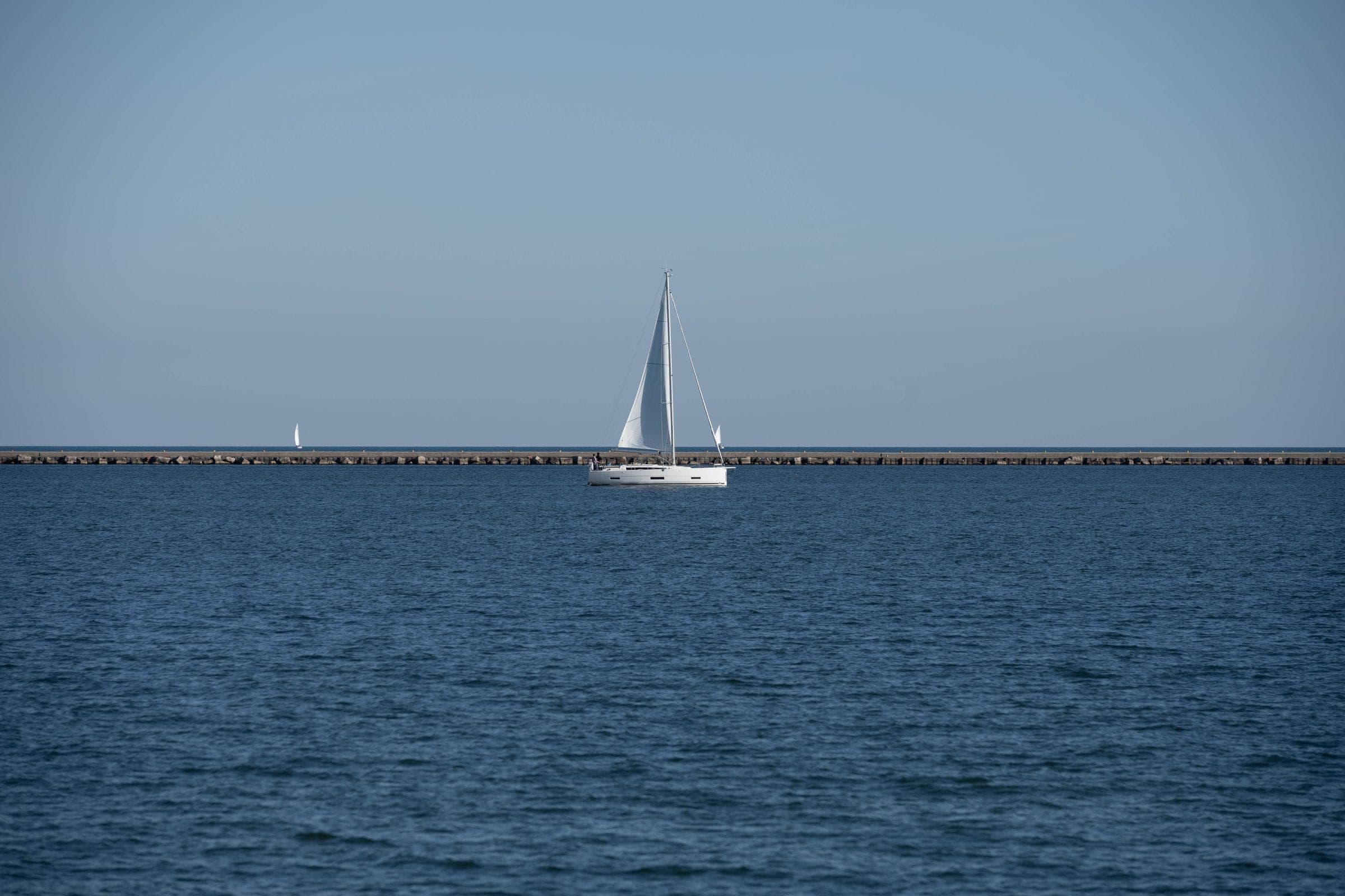 A single sailboat on flat Great Lakes water under an open sky