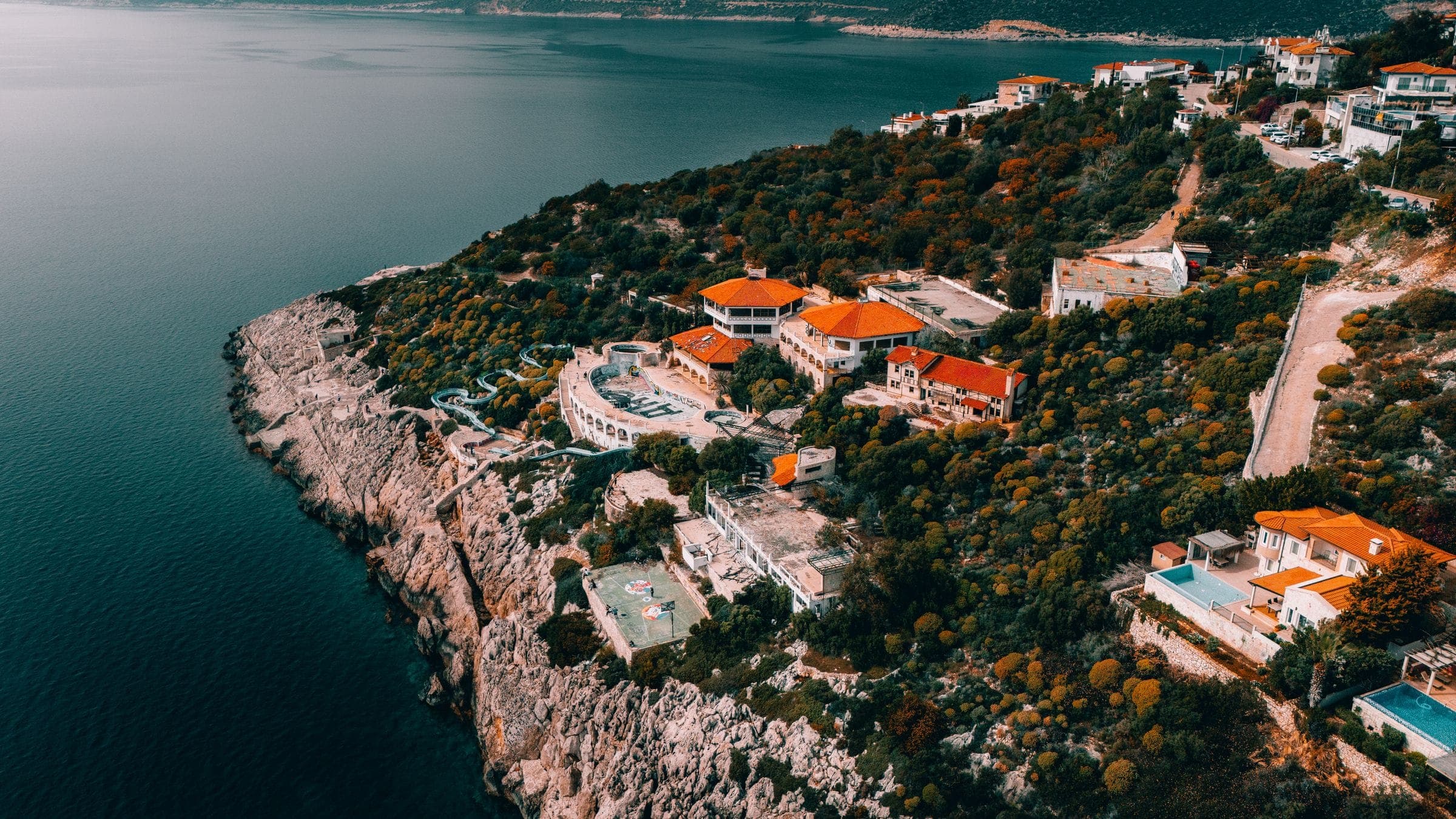 A wooded headland of villas and terraces above a quiet bay at dusk