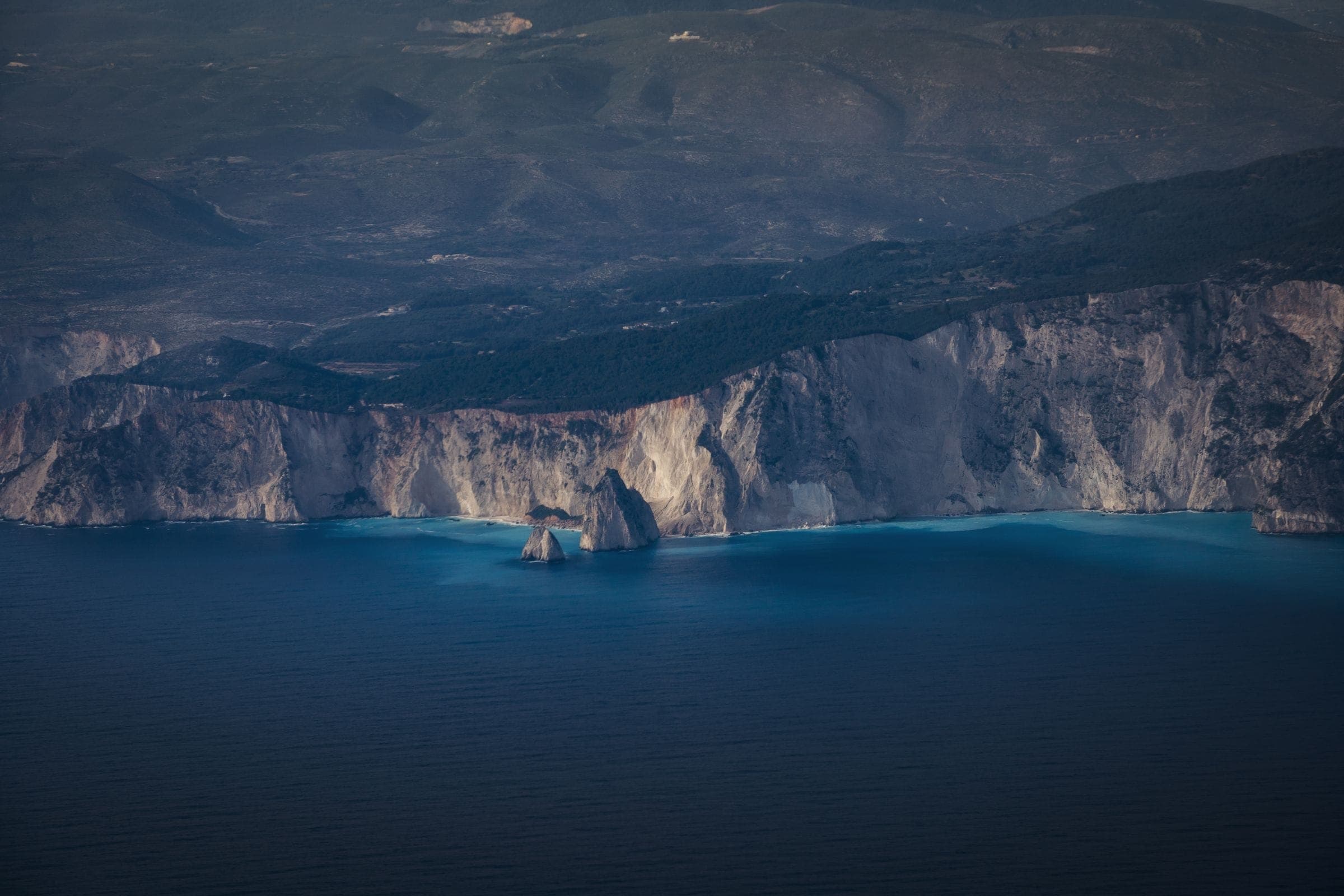 Dark limestone cliffs falling into deep blue water, photographed from the air