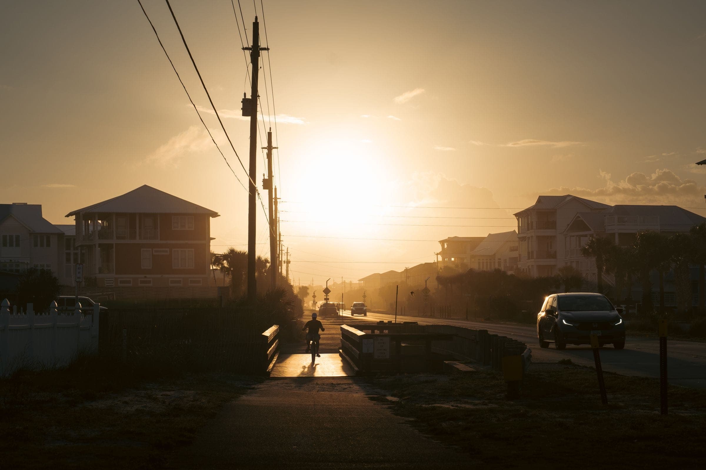 A quiet beach-town street at sunset, houses on stilts either side
