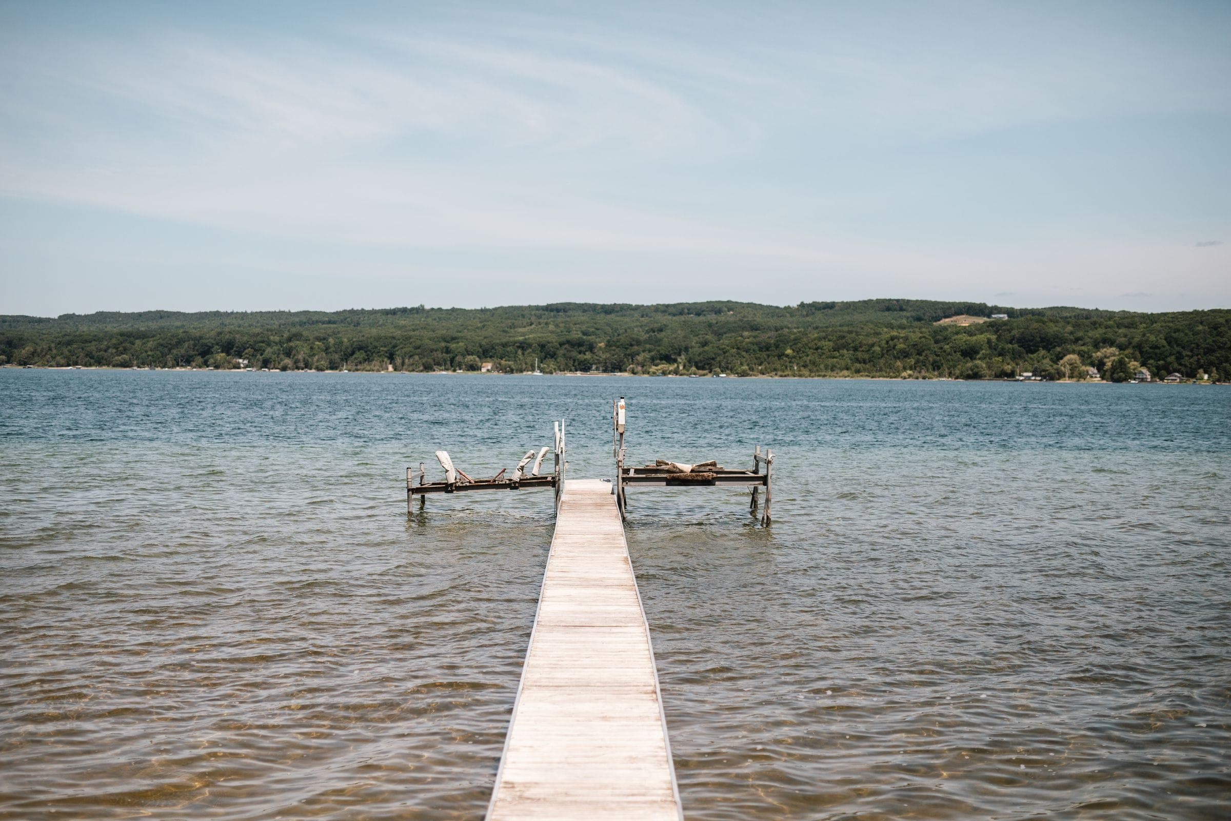 A wooden dock running out into a calm lake below a wooded shore