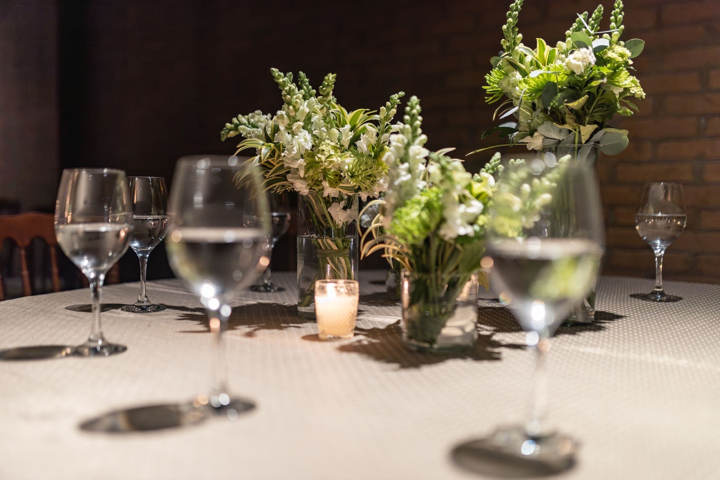 A dinner table laid with glassware and low garden flowers