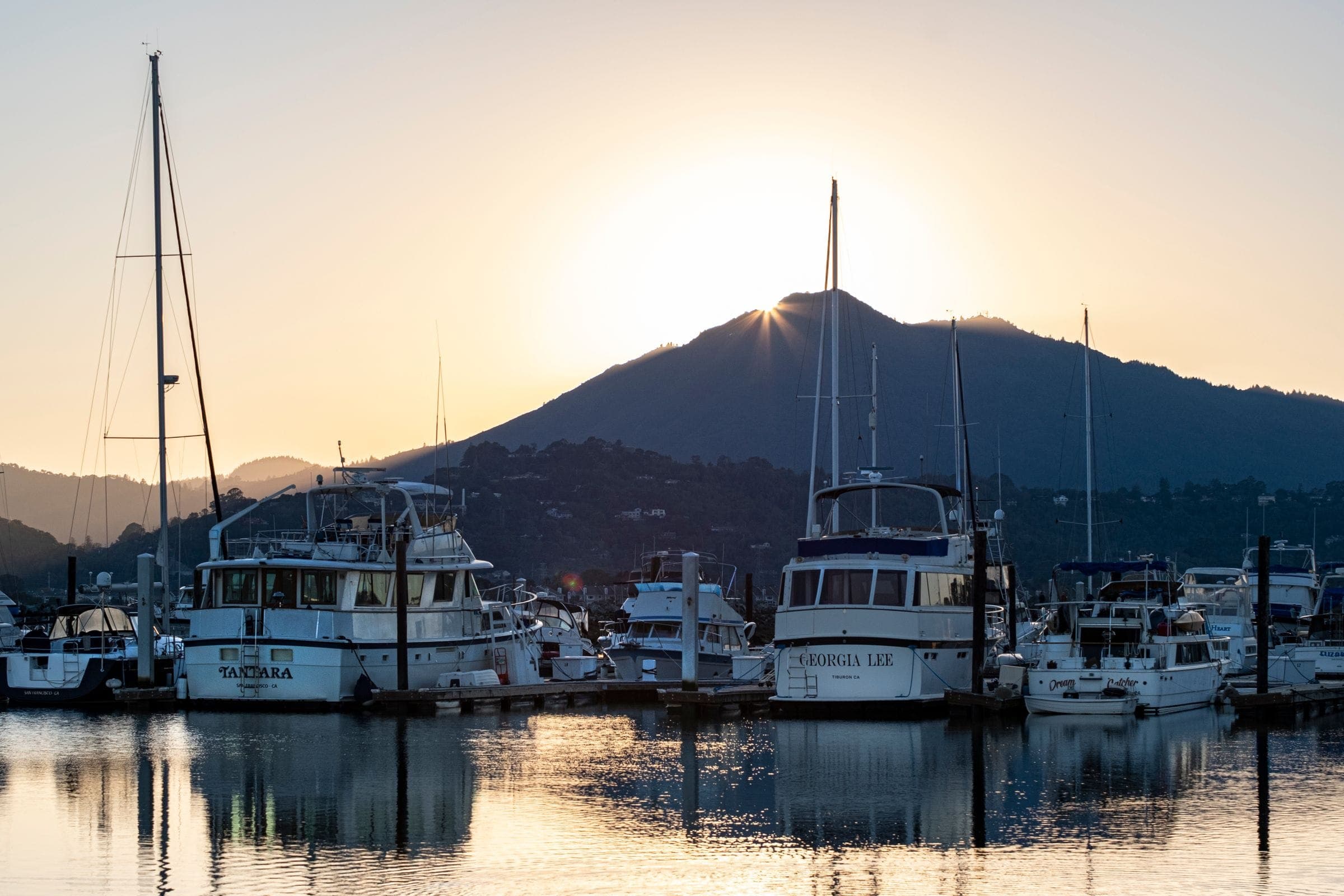 Boats at their moorings as the sun comes up behind the headland