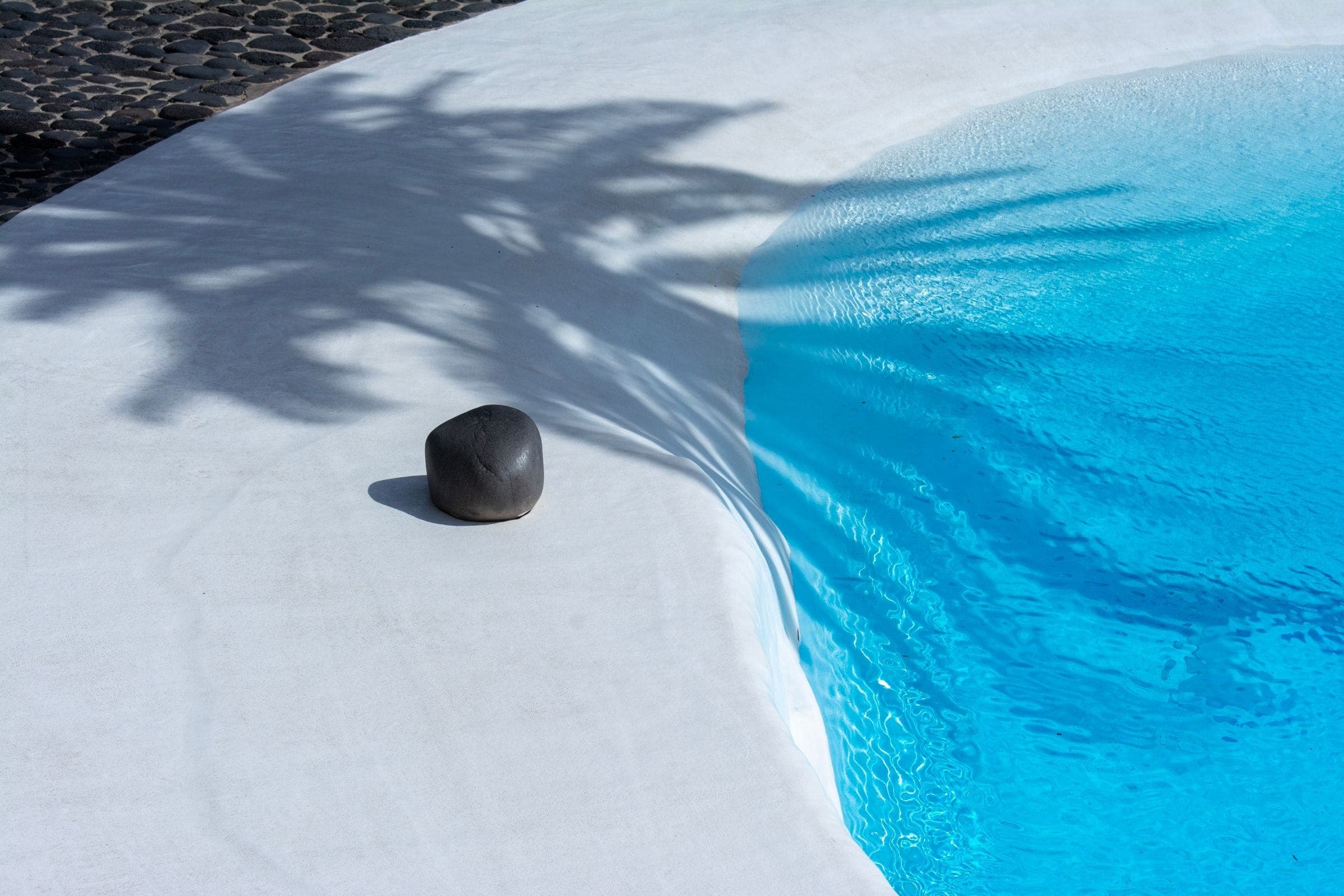 The curved edge of a swimming pool and its shadow on pale stone
