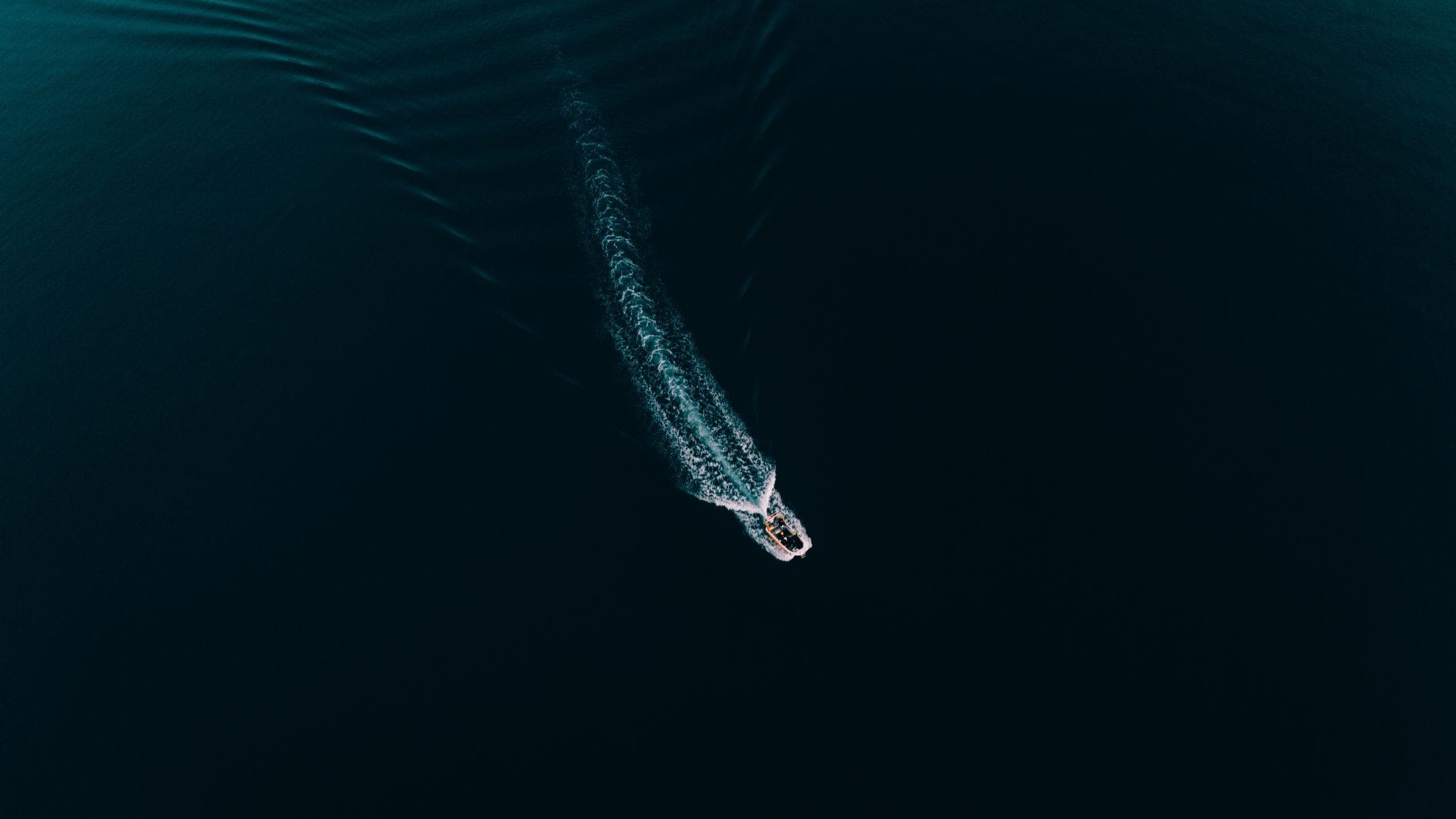 A single motor yacht drawing a wake across deep green water, seen from above