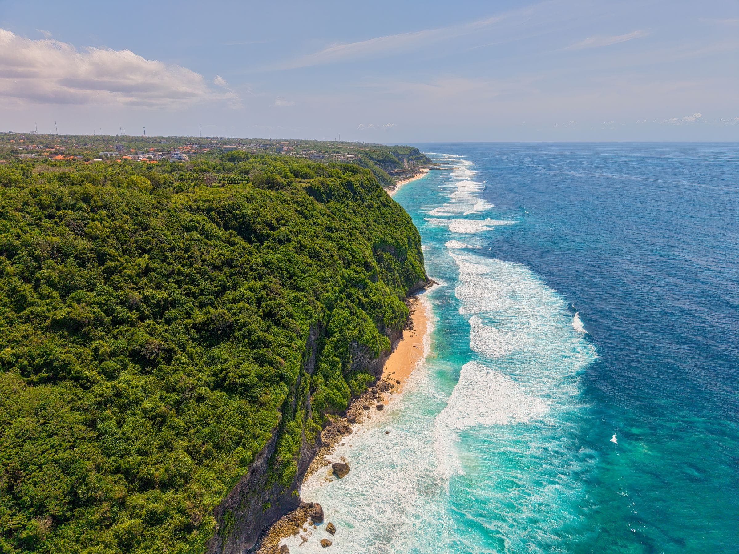 Surf along a green headland and a long empty beach, seen from the air
